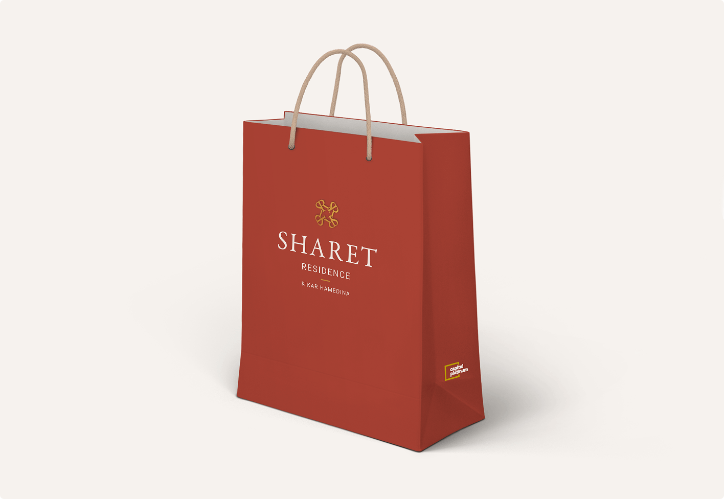 שקית קניות אדומה עם הכיתוב "SHARET RESIDENCE" ולוגו זהוב מודפסים עליה, ושתי ידיות חומות בהירות בחלק העליון.